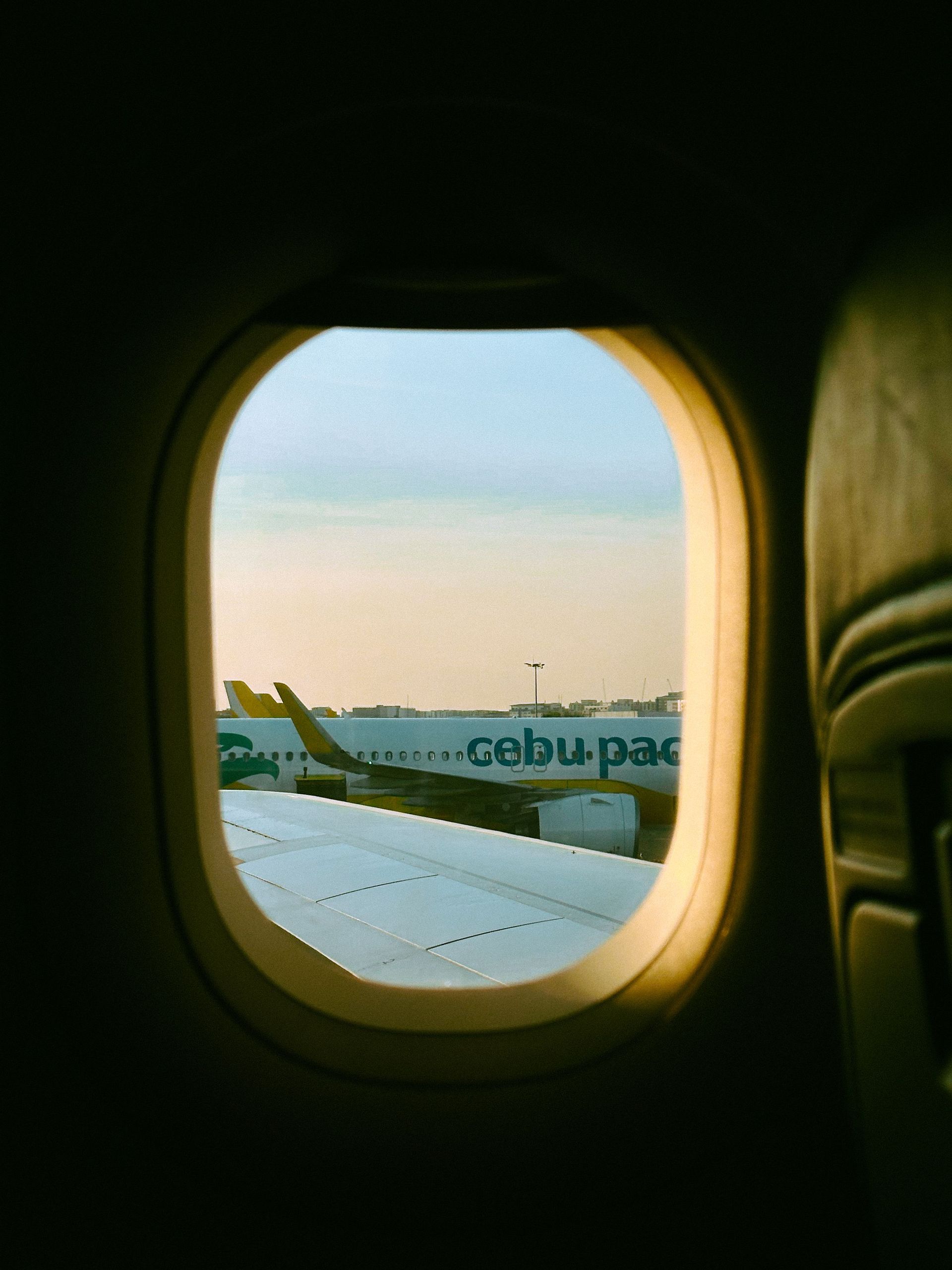 View through an airplane window of a Cebu Pacific wing and logo at sunset