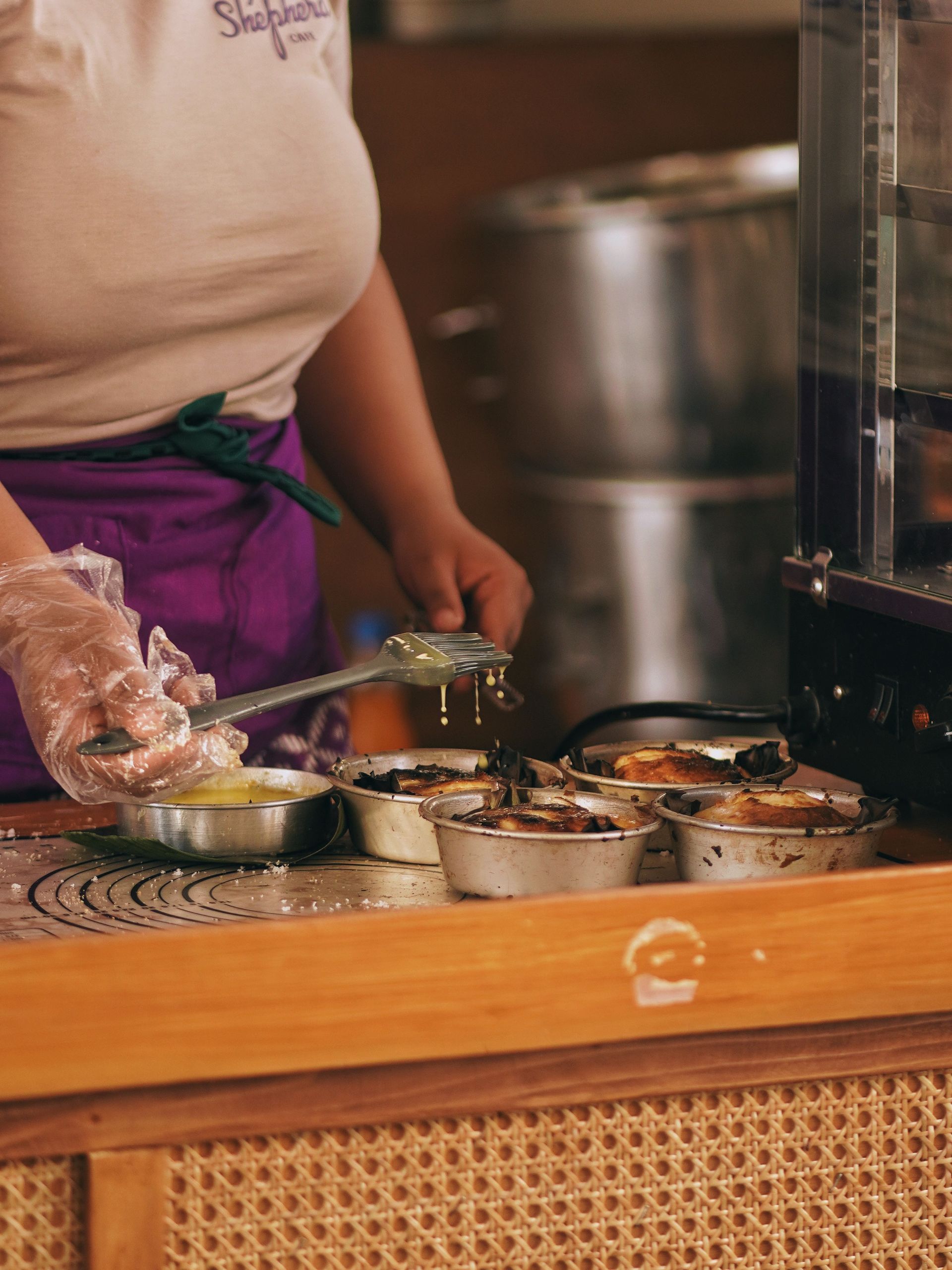Person serving food at a counter with metal dishes and a purple apron