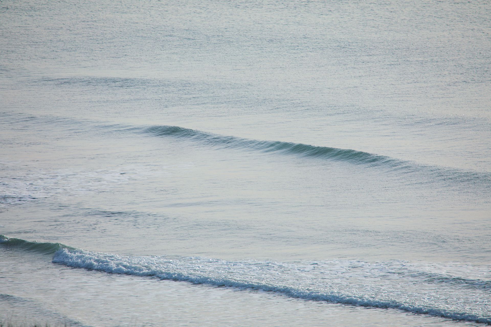 Gentle ocean waves rippling across a calm, pale blue-gray sea