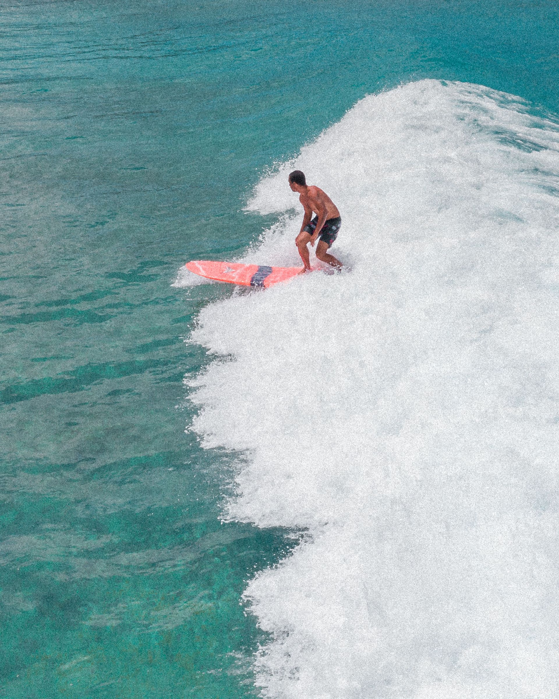 Surfer riding a pink board on a large white wave in turquoise water