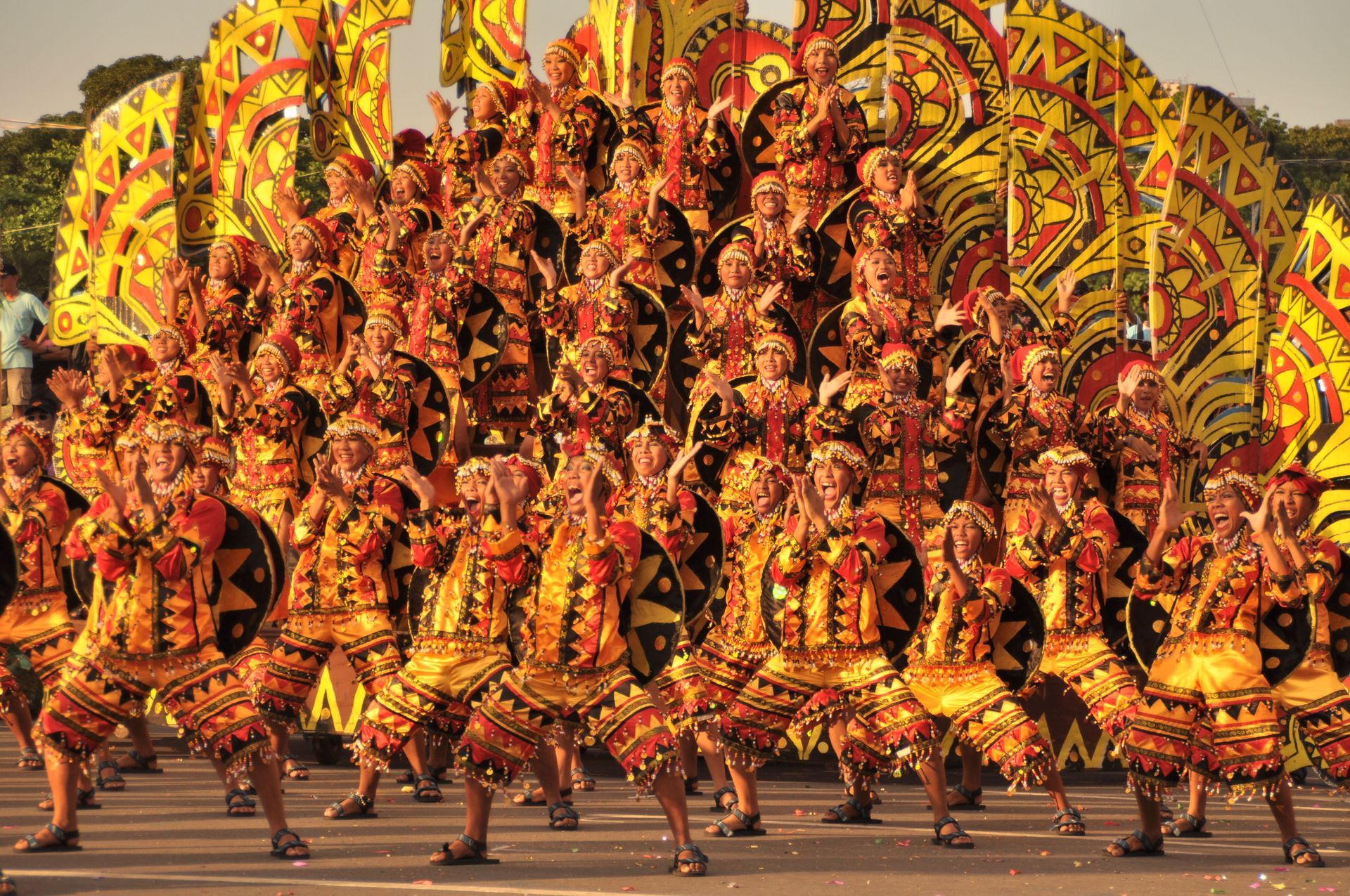 Large group of dancers in ornate red and gold costumes performing a synchronized traditional dance outdoors