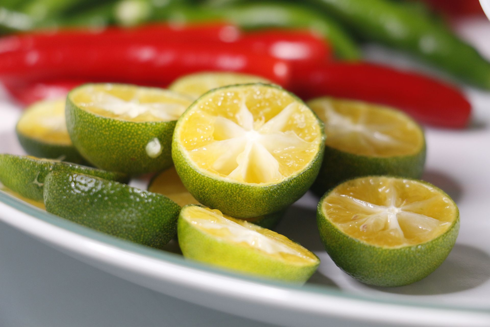 Sliced limes on a white plate with red chili peppers in the background