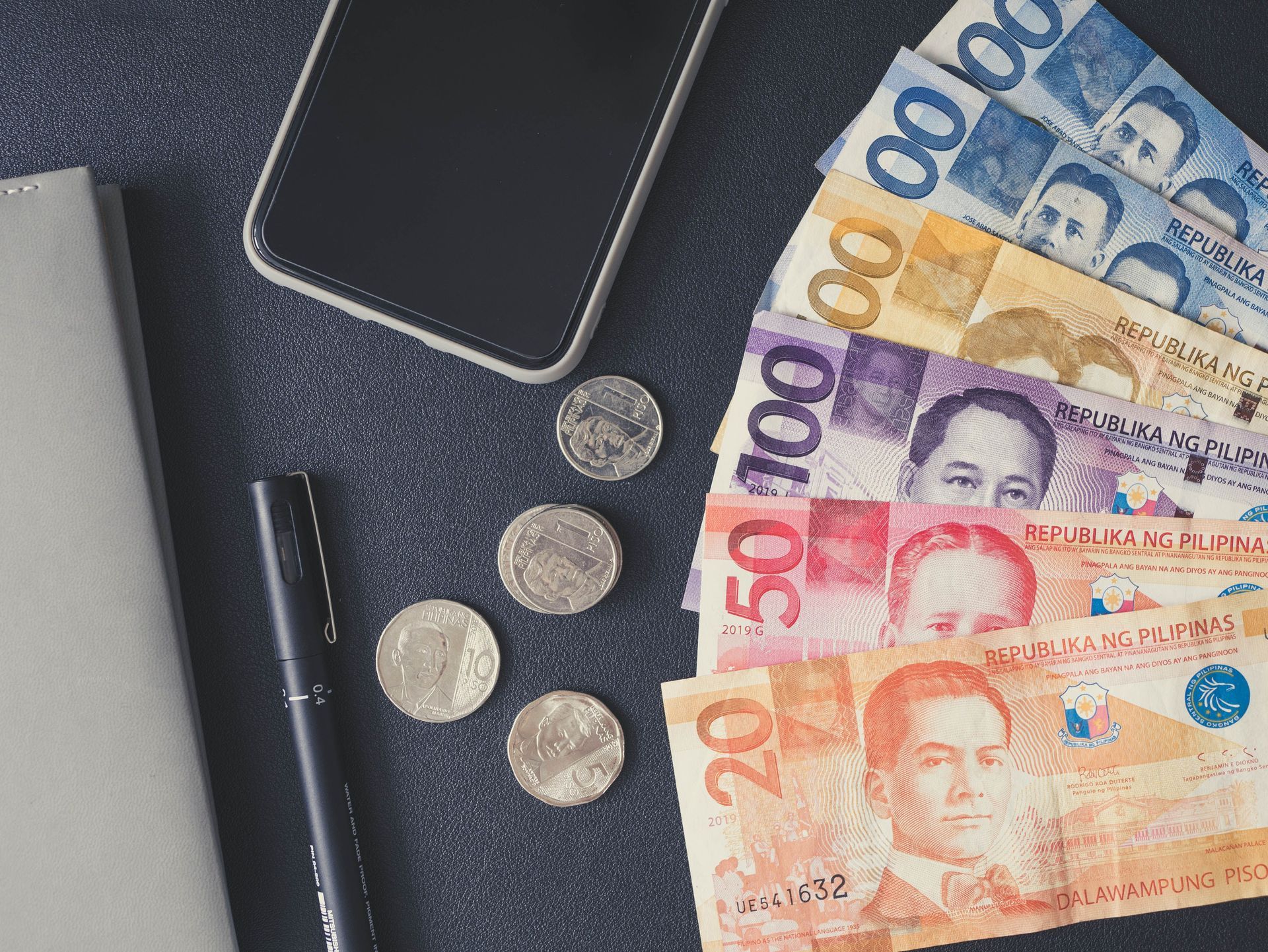 Wallet, smartphone, coins, and colorful banknotes on a dark surface.