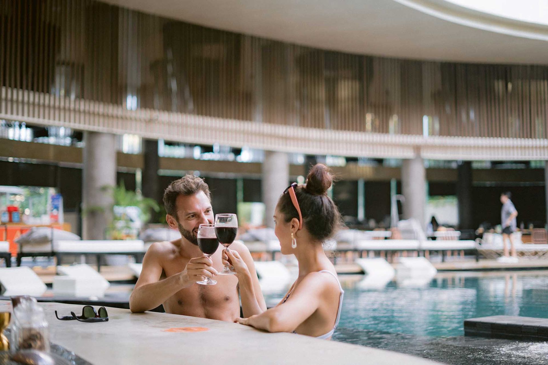 Couple relaxing in an indoor pool, holding drinks at a poolside ledge