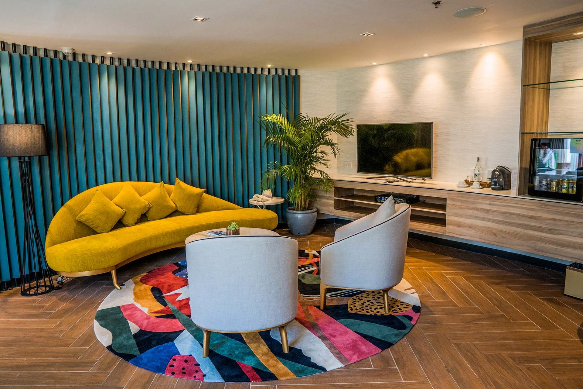 Living area of family-friendly Spectrum Suite featuring yellow curved sofa, turquoise wall panels, and colorful circular rug