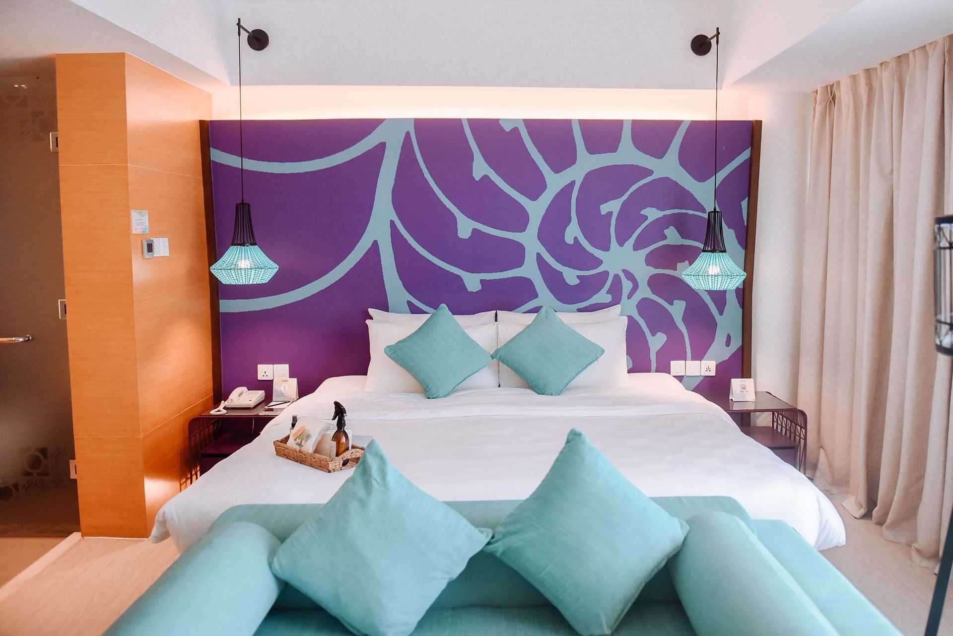 Vibrant hotel room with purple floral headboard and teal pillows at Hue Hot