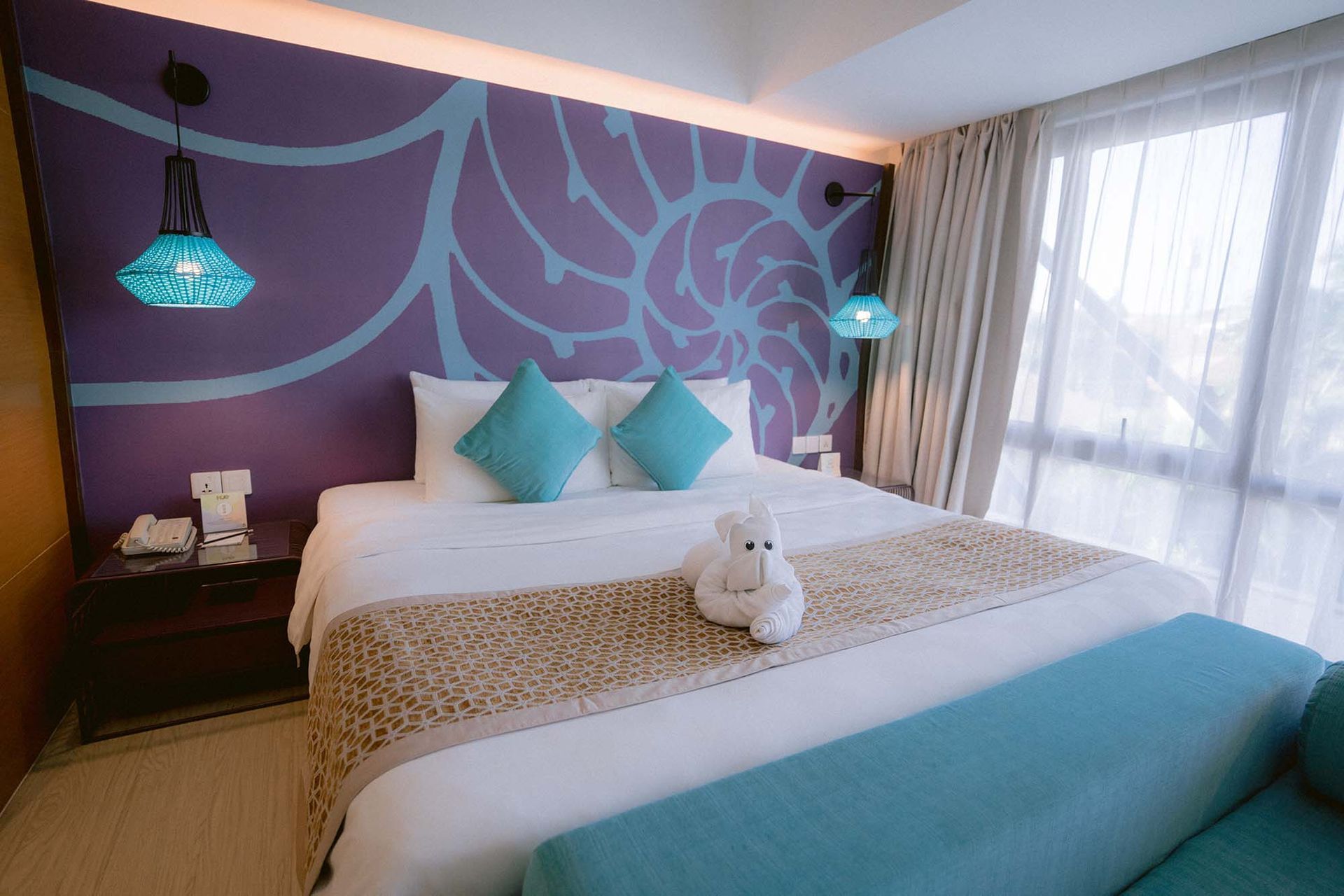 Stylish hotel room with purple mural, teal accents, and towel art at Hue Ho