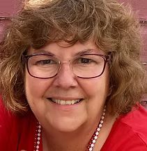 Woman with glasses smiling, wearing a red shirt and pearl necklace.