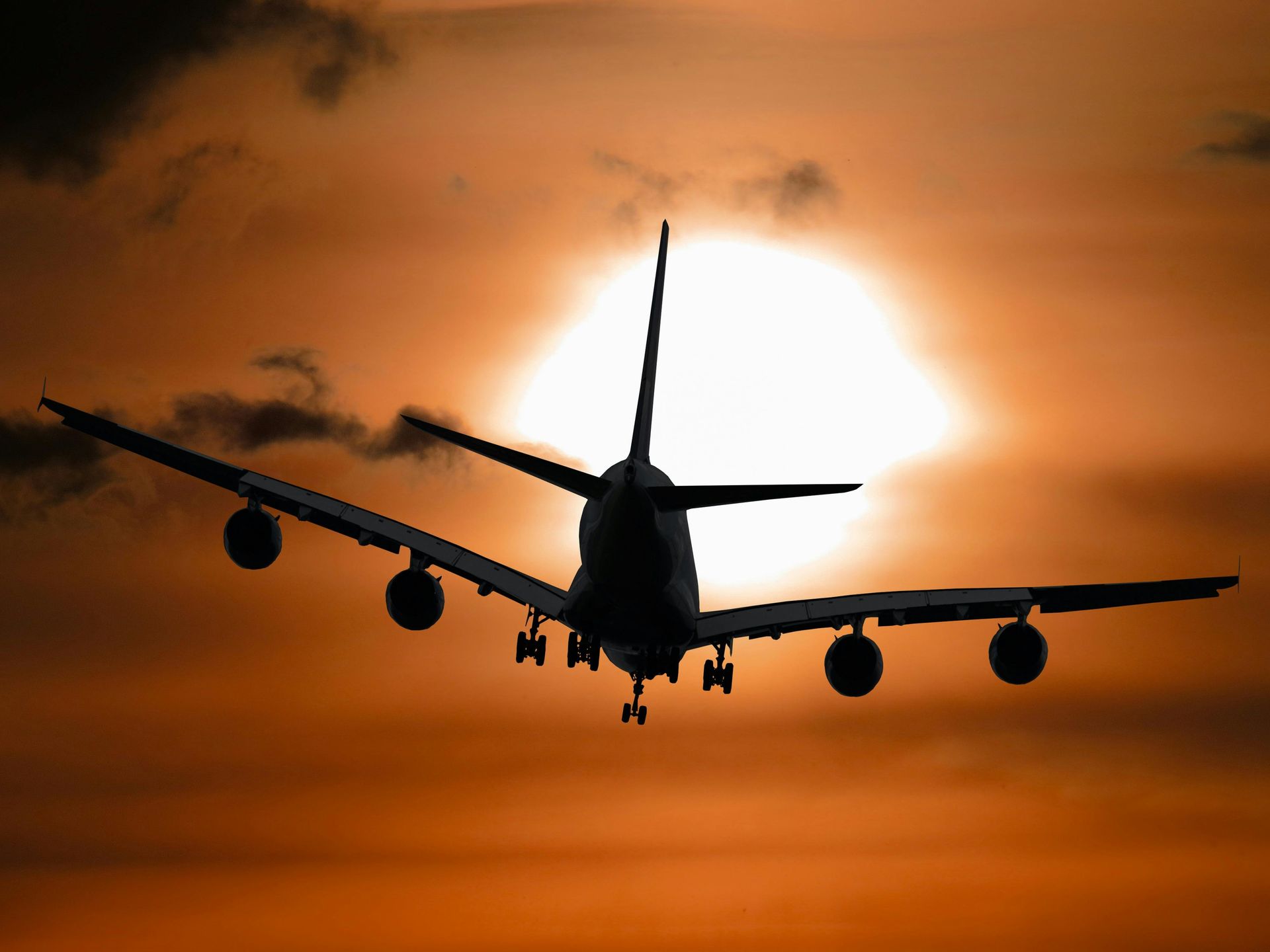 Airplane silhouetted against a fiery orange sunset, in flight.