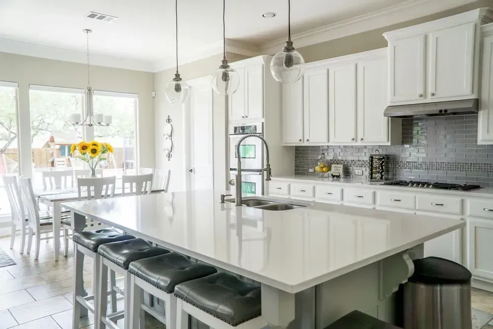 Bright modern kitchen with a large white island, pendant lights, and dining area by a sunlit window