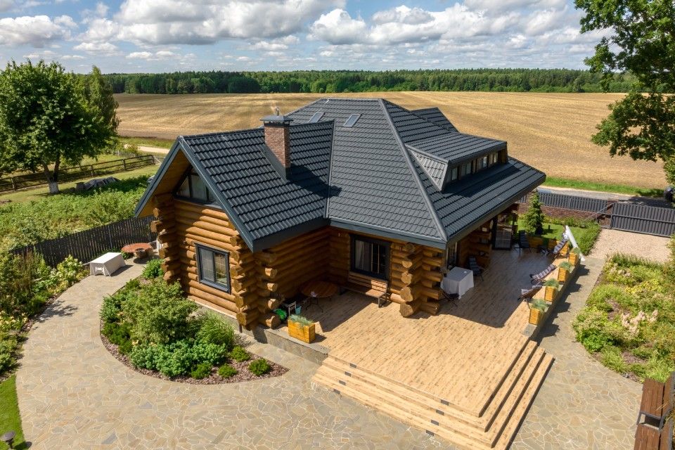 Log cabin house with dark roof and deck beside a rural field under a cloudy sky