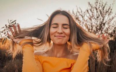 A woman in a yellow sweater is holding her hair in a field.