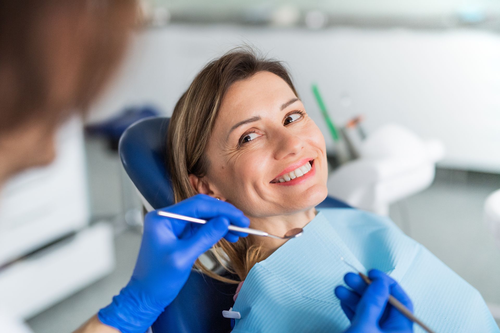 Dentist examining a smiling patient in a dental chair with blue gloves and bib