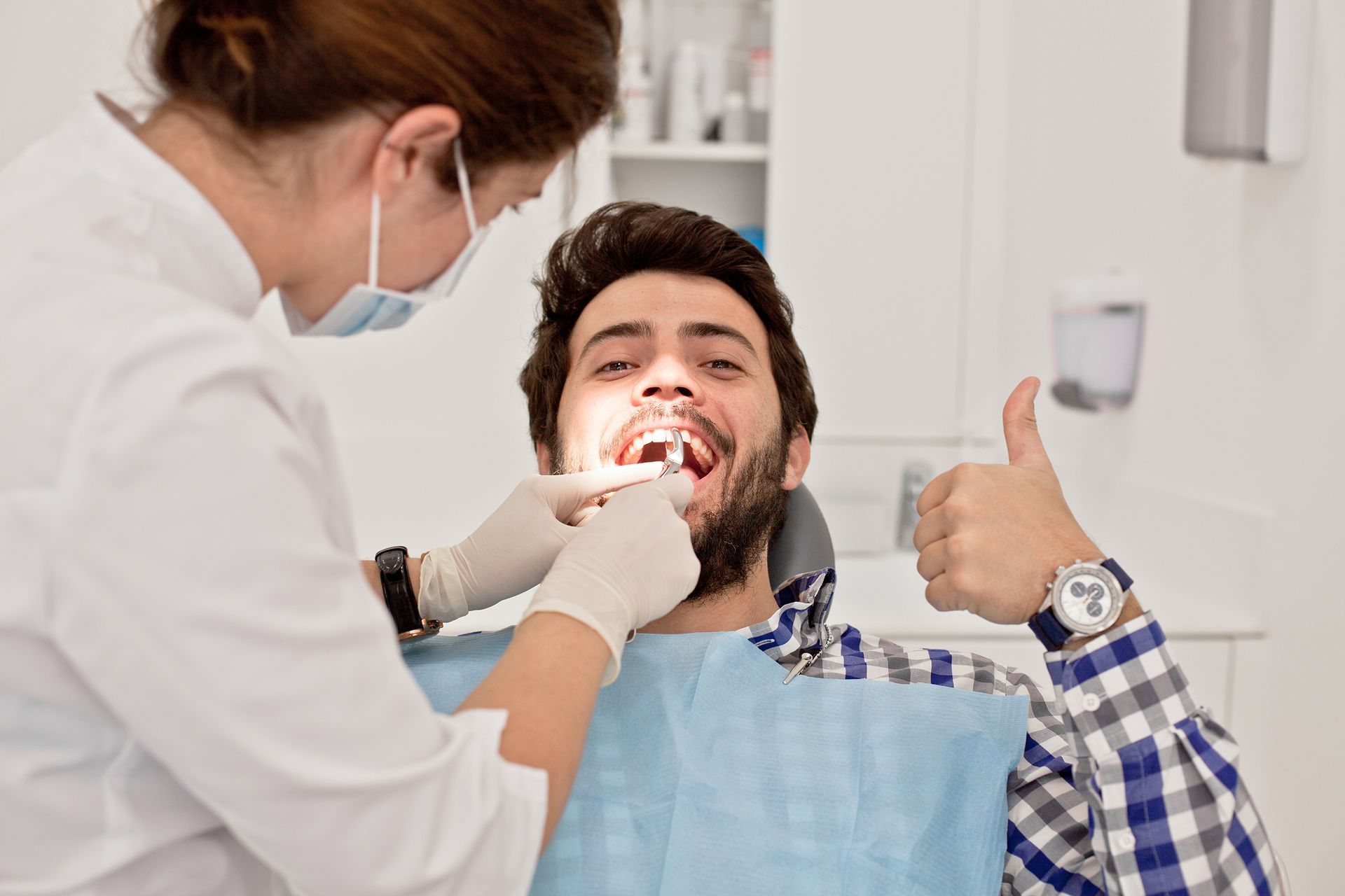 Dentist examining smiling patient giving a thumbs-up in a clinic chair