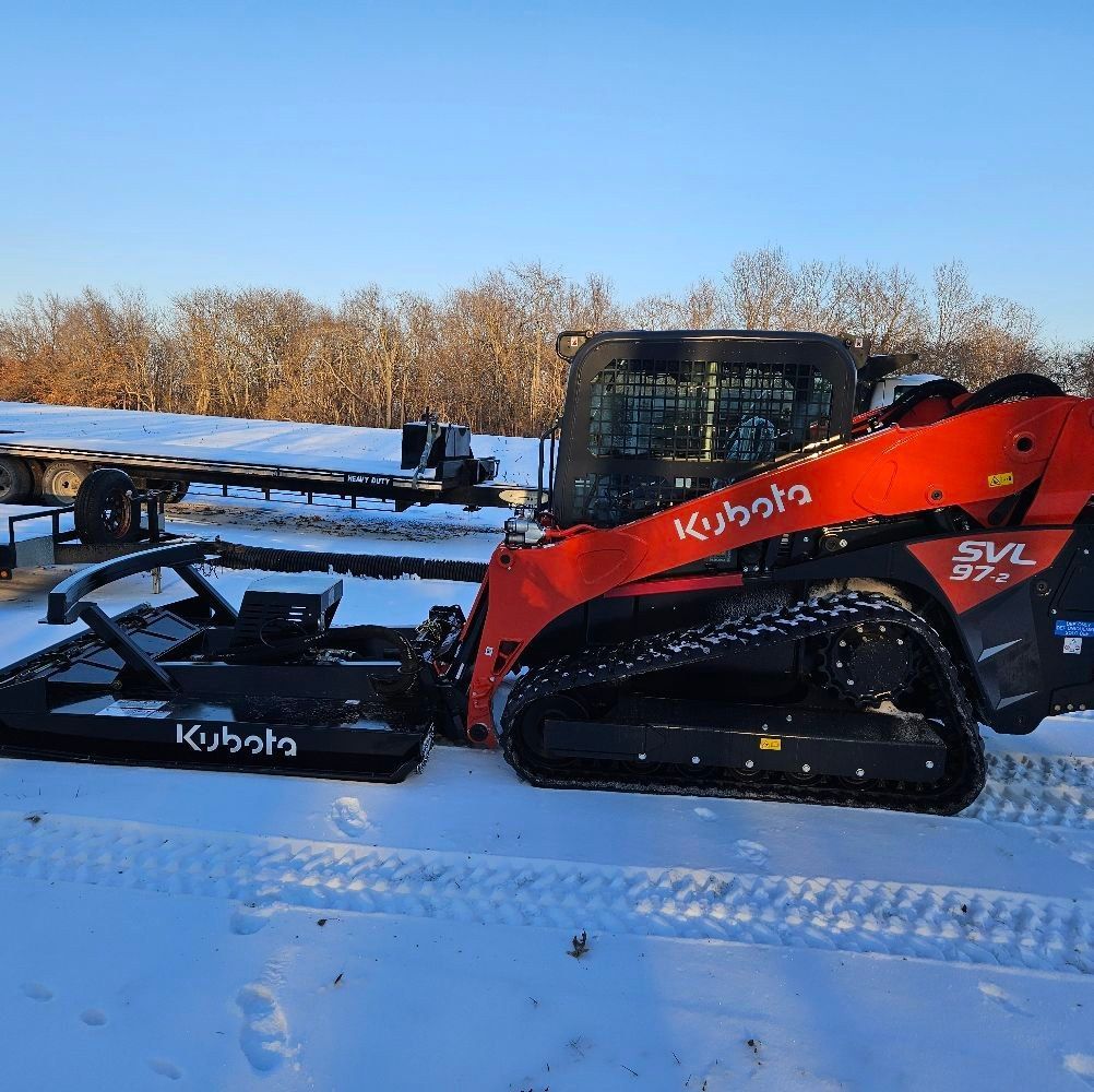An orange Kubota SVL 97-2 track loader with a brush cutter attachment parked in a snowy, rural field.