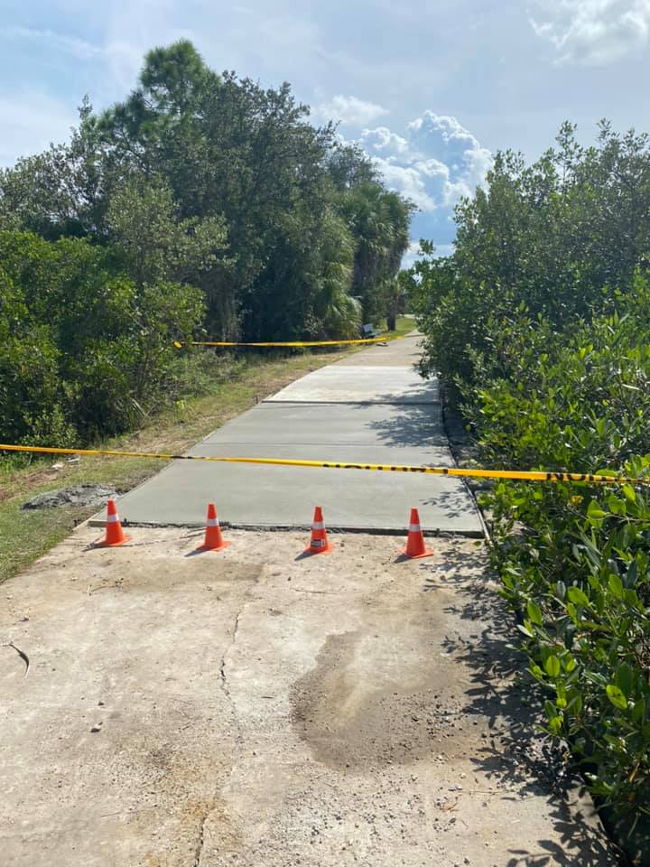 Pathway repair in progress; orange cones and caution tape block the way. Fresh concrete section on the path.