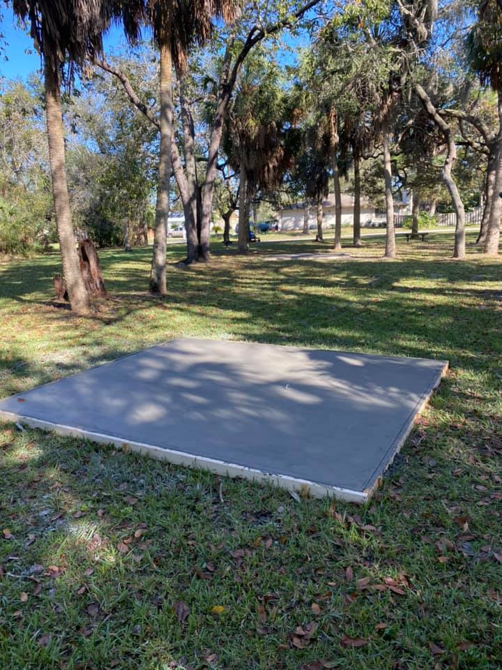A rectangular concrete slab on a grassy lawn, trees in the background under a blue sky.
