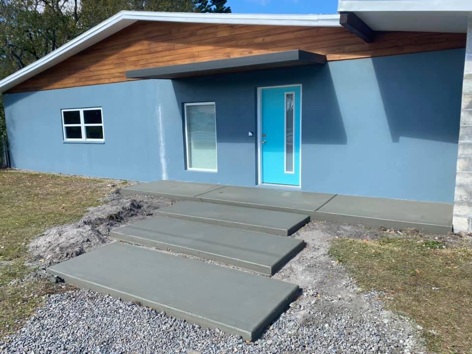 Steps lead up to a blue house with a teal door and wooden accents.