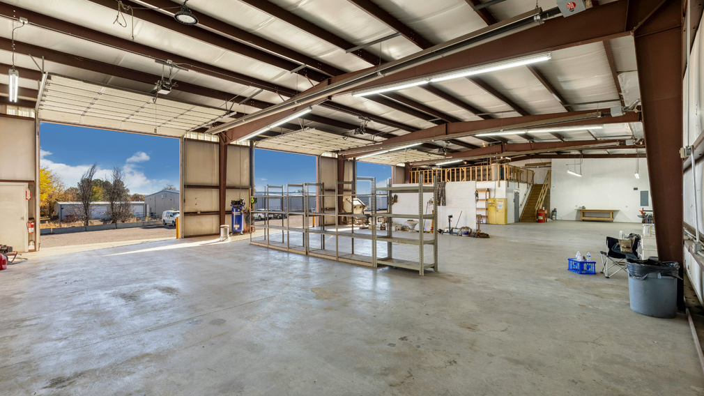 Large unfinished warehouse interior with concrete floor, exposed beams, and sunlight through open doors.