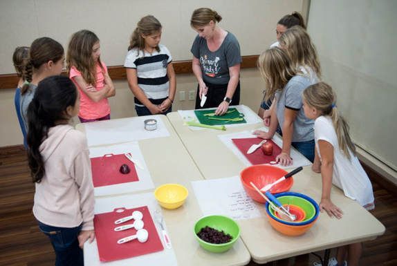 A group of children are standing around a table with bowls of food.
