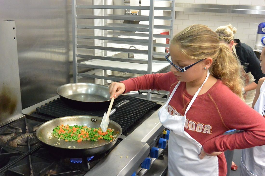 A girl wearing a red shirt that says boston is cooking vegetables in a pan