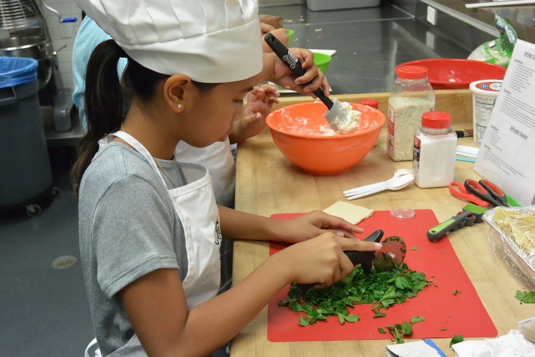 A girl in a chef 's hat is cutting vegetables on a cutting board