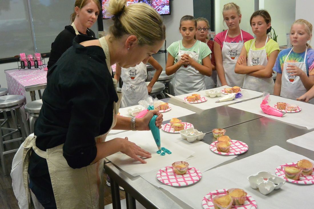 A woman is decorating cupcakes in front of a group of children.