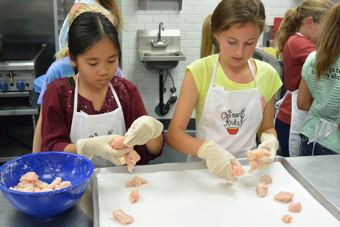 Two young girls are preparing food in a kitchen.