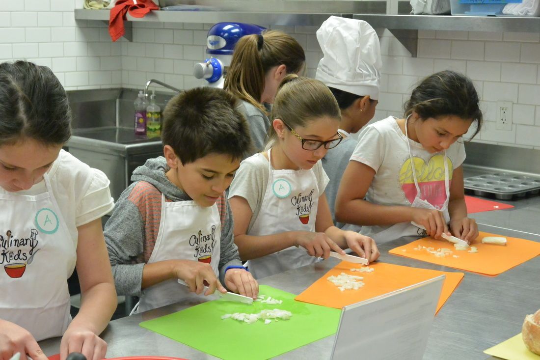 A group of children are sitting at a table in a kitchen cutting vegetables.