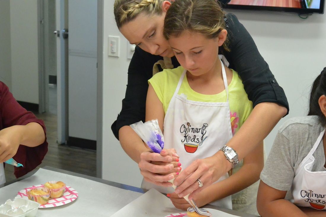 A woman is helping a young girl decorate a cake.