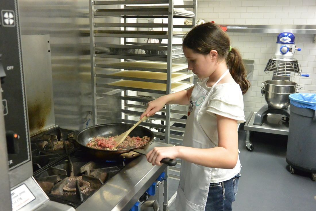 A young girl is stirring food in a frying pan in a kitchen