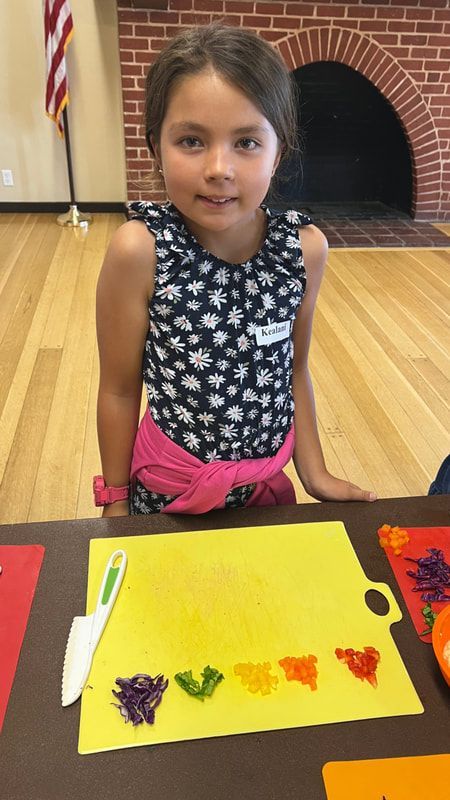 A little girl is sitting at a table with a cutting board and crayons.