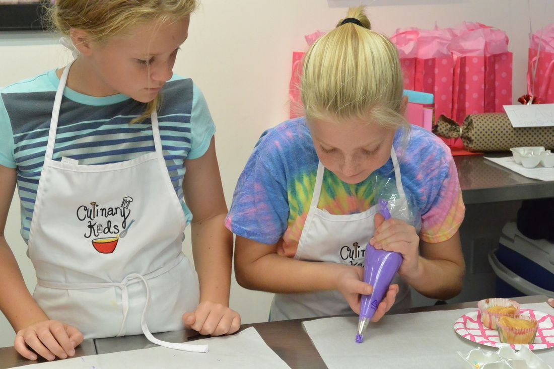 Two young girls are sitting at a table decorating a cake.