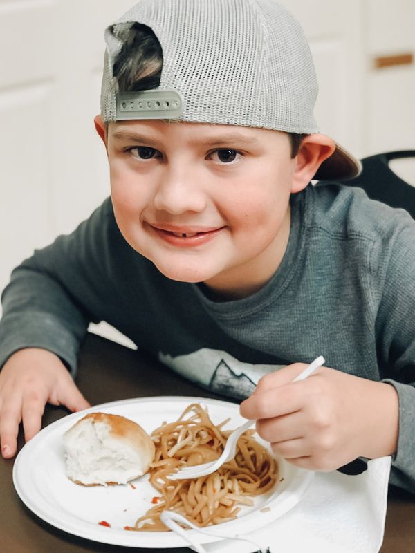 A young boy wearing a hat is eating spaghetti with a fork
