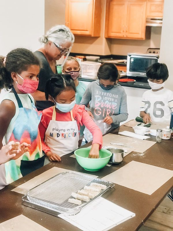 A group of children wearing face masks are sitting at a table in a kitchen.