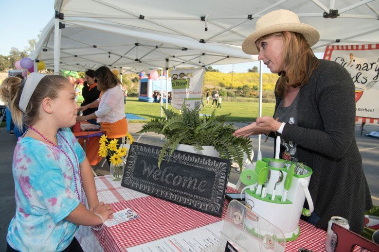 A woman is talking to a little girl at a table with a welcome sign on it.