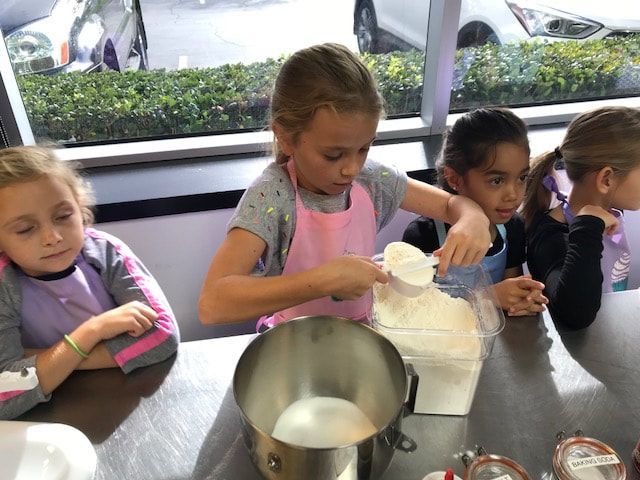 A group of young girls are sitting at a table preparing food