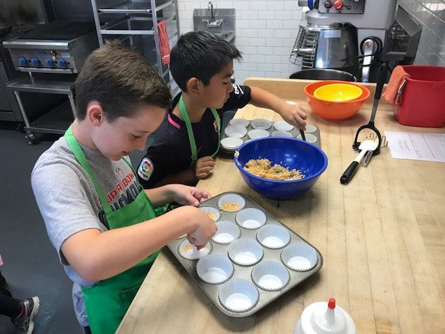 Two young boys are making cupcakes in a kitchen.