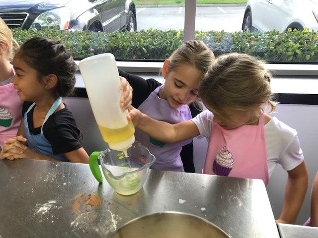 Three little girls are pouring liquid into a measuring cup