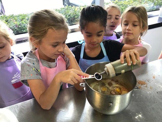 A group of young girls are mixing ingredients in a bowl.