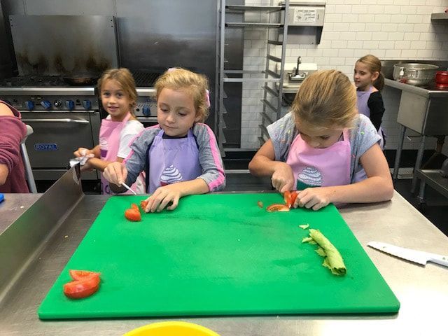A group of young girls are cutting vegetables on a green cutting board.
