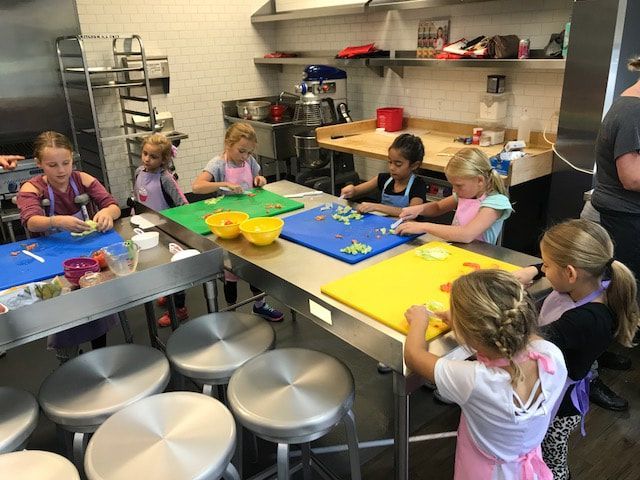 A group of young girls are cutting vegetables on cutting boards in a kitchen.