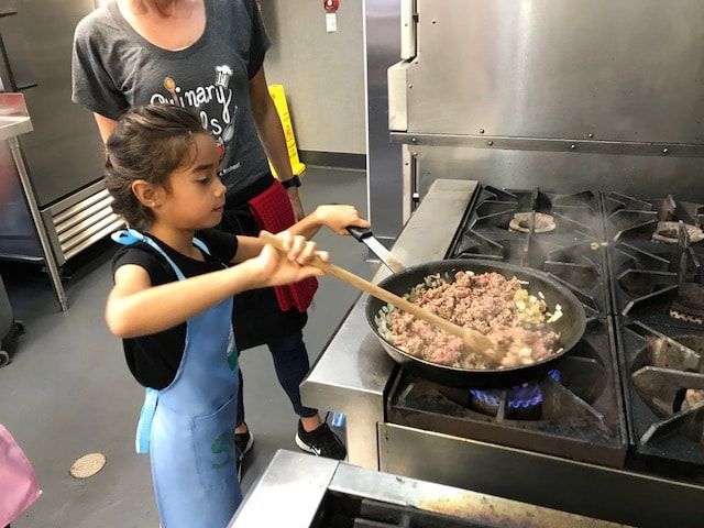 A little girl is stirring food in a frying pan on a stove.