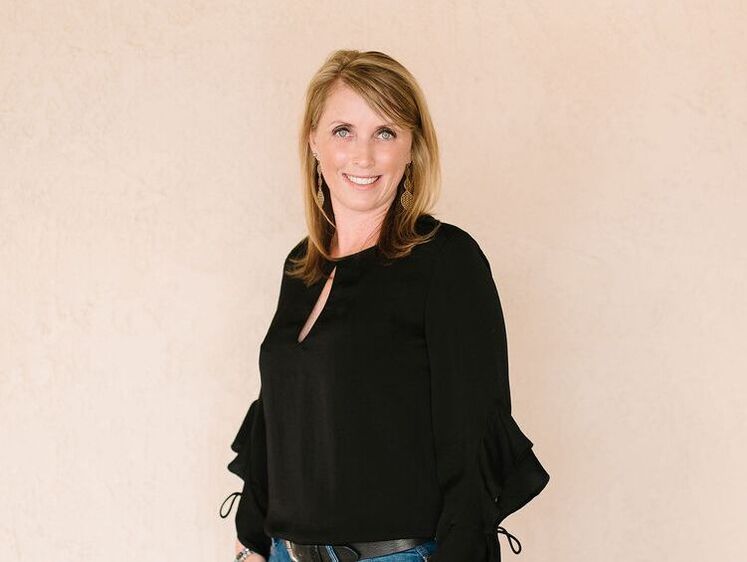 A woman in a black top and jeans is smiling for the camera.