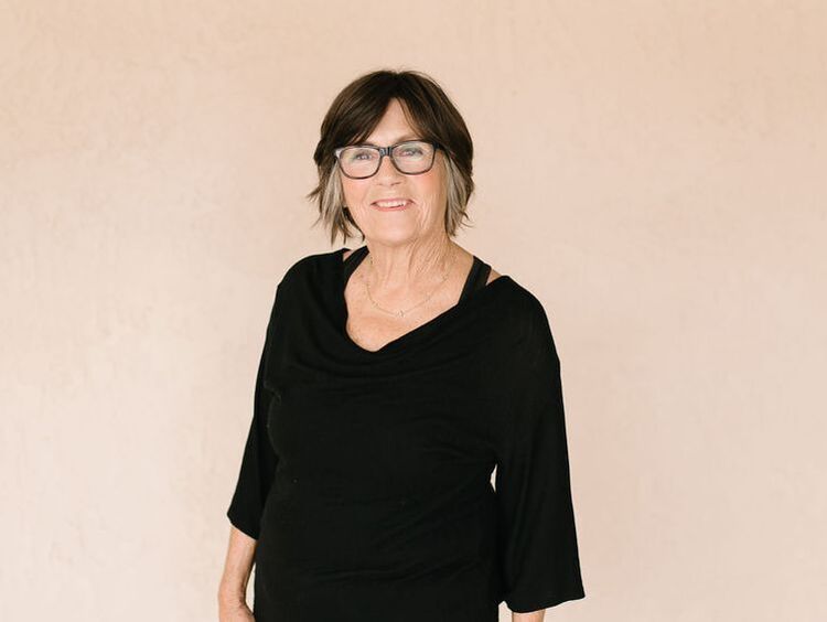 A woman wearing glasses and a black shirt is standing in front of a beige wall.