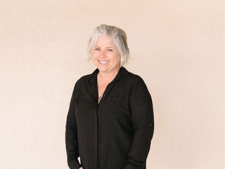 A woman with gray hair is wearing a black shirt and smiling.