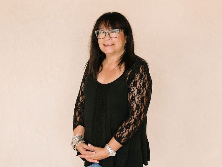 A woman wearing glasses and a black top is standing in front of a wall.