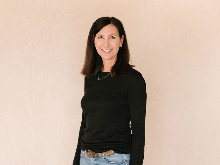 A woman in a black shirt and jeans is smiling for the camera.