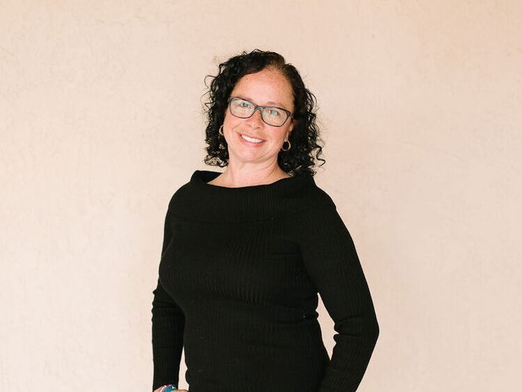 A woman wearing glasses and a black sweater is smiling for the camera.