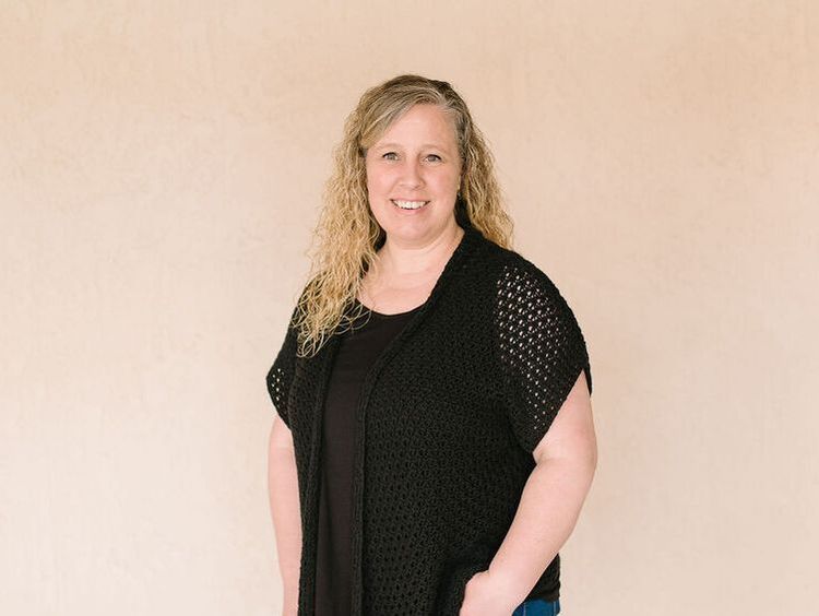 A woman wearing a black vest and a black shirt is standing in front of a beige wall.